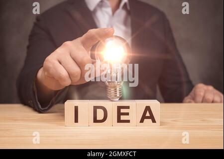 Hand of businessman holding illuminated light bulb, idea, innovation and inspiration concept. wooden cubes with IDEA text. Concept new idea with innov Stock Photo