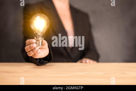 Business women holding light bulbs, new ideas with innovative technology and creativity. Woman hand holding light bulb on wooden desk. Concept new ide Stock Photo