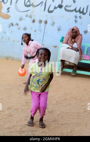 Aswan, Egypt - 3 December 2010; Two small girsl lost in play with a battered old ball, whilst an old woman looks on. Shot in a small Nubian village on Stock Photo