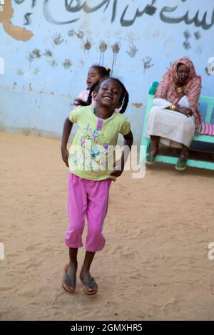 Aswan, Egypt - 3 December 2010; Two small girsl lost in play with a battered old ball, whilst an old woman looks on. Shot in a small Nubian village on Stock Photo