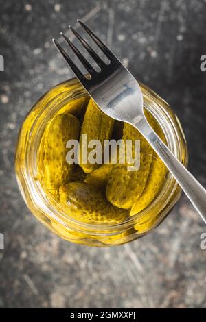 Small pickles. Marinated pickled cucumbers in jar on kitchen table. Top view. Stock Photo