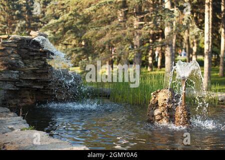 Beautiful pond with fountain in park made in handmade of stones and evergreen plant Stock Photo