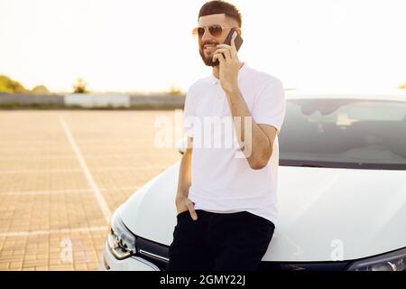 Handsome young business man talking on a mobile phone in the city near a white car, a man in glasses posing near a car in the city outdoors Stock Photo