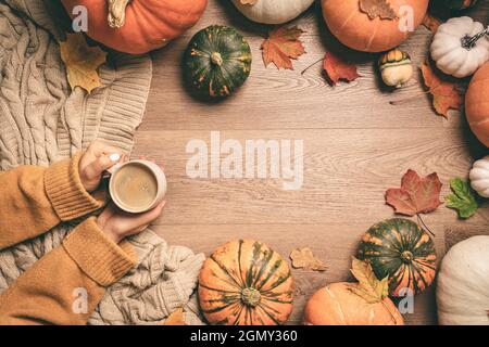 Womans Hands holding warm coffee with pumpkins and colorful leaves background top view. Stylish autumn flat lay. Hello fall. Cozy warm image Stock Photo