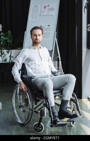 serious disabled businessman in wheelchair looking at camera near blurred flip chart Stock Photo