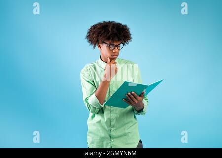 Learning concept. African american male student reading something in notepad, preparing for exams, blue background Stock Photo