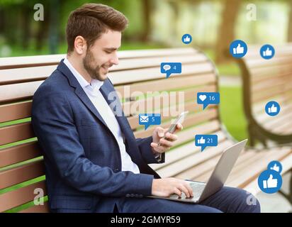 Smiling successful young european businessman chatting outdoors, working and texting clients on bench Stock Photo