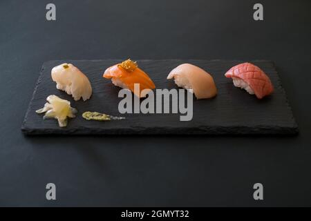 Sushi set served on black tray. Various kinds of sushi pieces served on black slate with ginger. Japanese traditional food on black background. Stock Photo