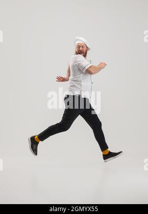 Portrait of cook, chef man in uniform running to kitchen isolated on white background. Concept of job, occupation, humor. Stock Photo