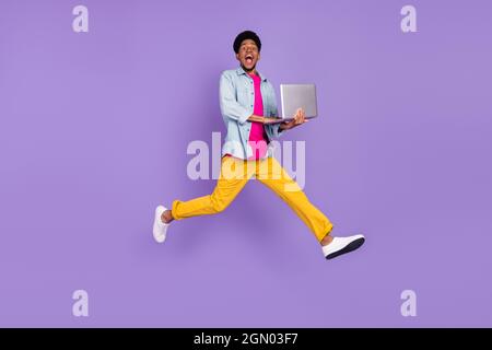 Photo of programmer guy jump hold netbook hurry late wear blue shirt pants shoes isolated purple color background Stock Photo
