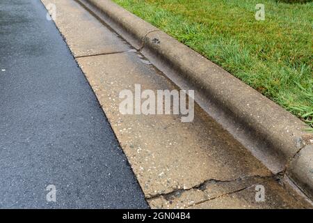 Small stream of rainwater next to an extruded concrete curb between a wet, asphalt road surface and green grass landscaping, horizontal aspect Stock Photo