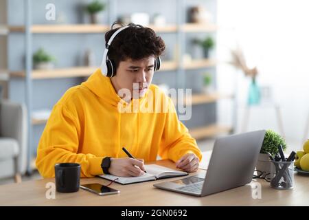 Focused asian man working on laptop and writing Stock Photo