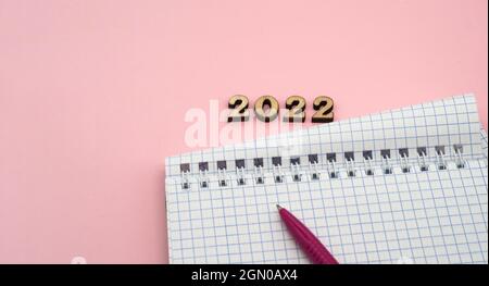 Wooden numbers 2022. Notepad on a spring. Notepad and Pen on Pink. Pink Pen. Spiral spiral checkered sheets. Stock Photo