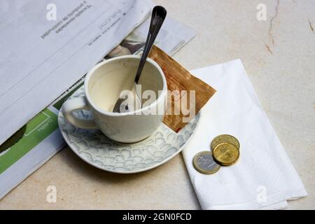 Close-up of a cup of coffee or tea in a bar, next to it is a newspaper and some coins with the price of the drink or the tip for the waiters Stock Photo