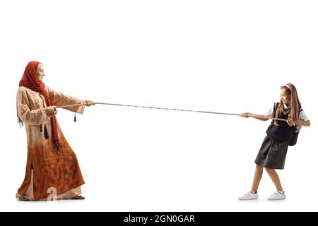 Full length profile shot of a schoolgirl pulling a rope from one side and a woman with a hijab on the other side isolated on white background Stock Photo