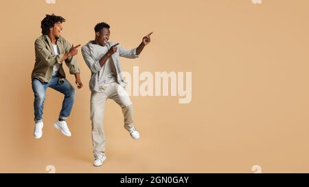 Look At This. Joyful Black Guys Pointing Aside While Jumping In Air Stock Photo