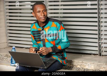 handsome african man sitting outside using a laptop and looking aside smiling Stock Photo