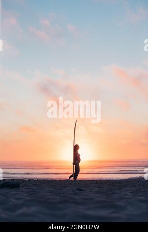 pregnant woman standing with surfboard on the beach, surfing, pregnancy, Portugal Stock Photo