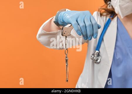 Doctor hands in handcuffs on red background, closeup. Woman hands in medical gloves handcuffed, coronavirus quarantine concept. Stock Photo