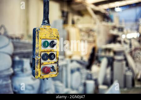Weathered yellow controller with buttons for remote operating overhead crane hanging in industrial workplace with blurred equipment Stock Photo