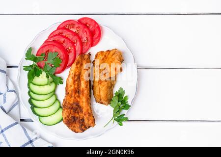 Top view of deep fried hake fish with vegetables served on a plate on white wooden background, copy space Stock Photo