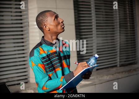 Handsome reflective young man holding notebook and pen looking up Stock Photo