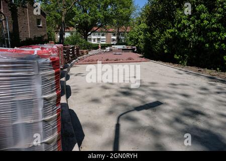 Construction of a cobblestone street. Pile of cobblestones with sand and signage signs, residential block, residential area, houses in the background. Stock Photo