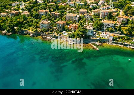 Beautiful villas near the coast of rocky beach in a small town Lovran, Croatia. Arial view of Lungomare sea walkway with transparent water. Stock Photo