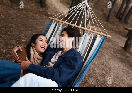Excited multiethnic couple hugging in hammock during weekend Stock Photo