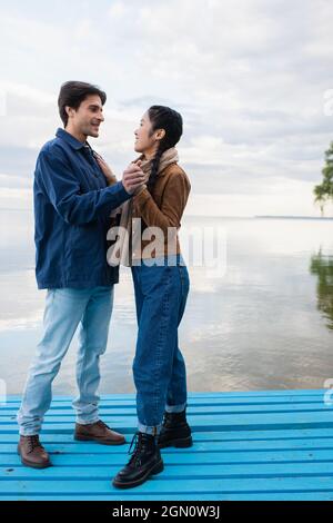 Side view of interracial couple holding hands on pier near lake Stock Photo