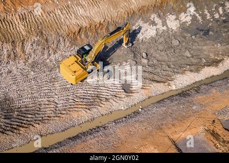 Heavy excavator ripping big stones from mountain ground with help of duty single shank excavator ripper, top down aerial photo Stock Photo