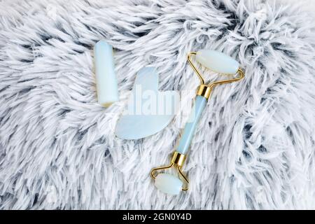 opal crystal facial roller and massage tool jade Gua sha on grey artificial fur background. Facial anti-age massage. Stock Photo