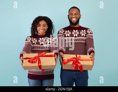 Happy african american couple stretching Christmas gifts to camera over blue studio background, celebrating New Year Stock Photo