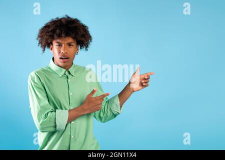 Emotional african american teenage guy pointing aside at empty space with two hands, blue background Stock Photo