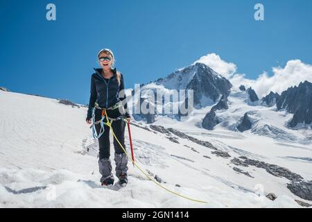 Happy cheerful sincerely laughing young female portrait in climbing harness, crampons, sunglasses, mountain team rope while she descending after succe Stock Photo