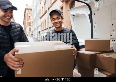 Two smiling coworkers unloading cardboard boxes from van for delivery Stock Photo
