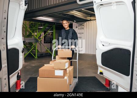 Smiling woman in uniform standing in warehouse with cart preparing for delivery Stock Photo