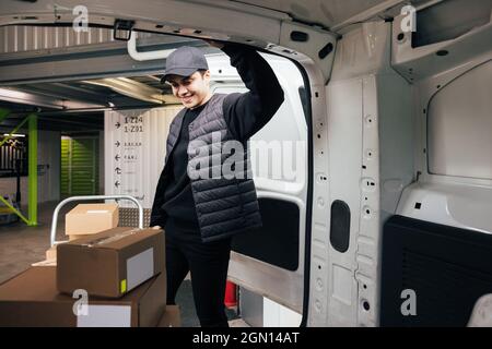 Confident courier leaning on van looking on cardboard boxes Stock Photo