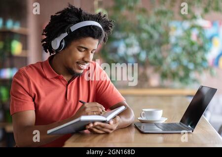 Young Black Guy Taking Notes While Studying Online With Laptop In Cafe Stock Photo