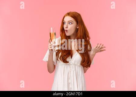 Wow this alcohol hits different. Amused and enthusiastic surprised redhead woman look amazed and wondered and glass with champagne, raising one hand Stock Photo