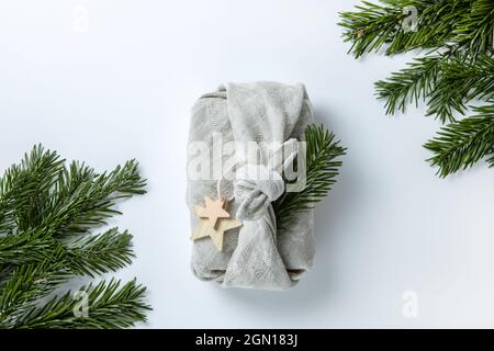 Zero waste Merry Christmas winter gift wrapping in traditional Japanese furoshiki style in linen fabric, decorated with natural green branches of fir