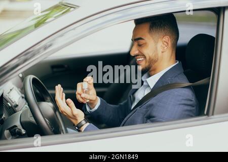 Cheerful businessman using disinfectant spray while sitting in car Stock Photo