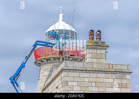 Workmen, using an articulated boom, repainting the lighthouse in Howth, Dublin, Ireland.. Stock Photo
