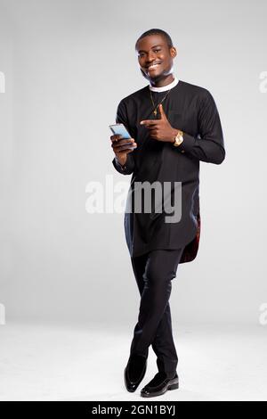 handsome young african man smiling while using his phone and pointing to it Stock Photo