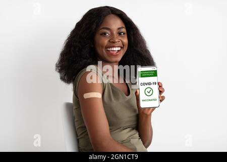 Vaccinated pretty black woman showing smartphone with vaccination certificate Stock Photo