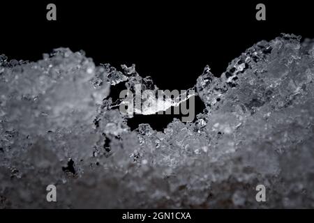 Super close up abstract image of slowly thawing snow. Minute detail of the ice crystals are visible, plain black background. Cold outdoor weather Stock Photo