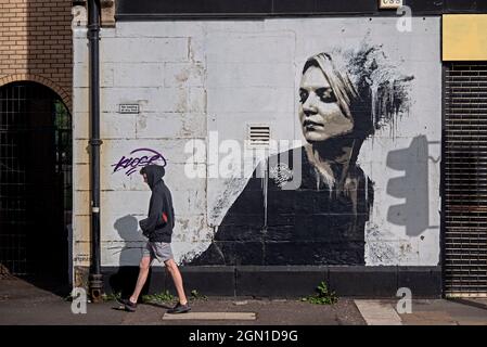 Young man walking by Woman In Black by James Klinge at Bridgegate, part of the Glasgow Mural Trail. Stock Photo