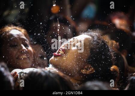 Kathmandu, Nepal. 21st Sep, 2021. Nepalese women struggle to drink homemade alcohol from the mouth of Deity Swet Bhairav as blessings during Indra Jatra festival.The annual festival, named after Indra, the god of rain and heaven, is celebrated by worshipping, rejoicing, singing, dancing and feasting in Kathmandu Valley to mark the end of monsoon season. Indra, the living goddess Kumari and other deities are worshipped during the festival. Credit: SOPA Images Limited/Alamy Live News Stock Photo