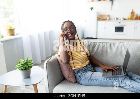 Pretty black woman freelancer talking on phone and using laptop Stock Photo