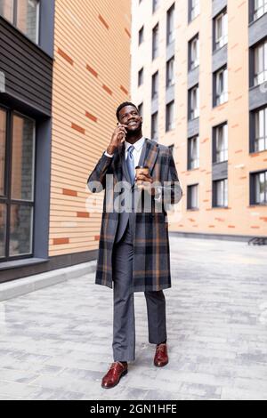 African american businessman with coffee to go having business call during break, walking outdoors Stock Photo